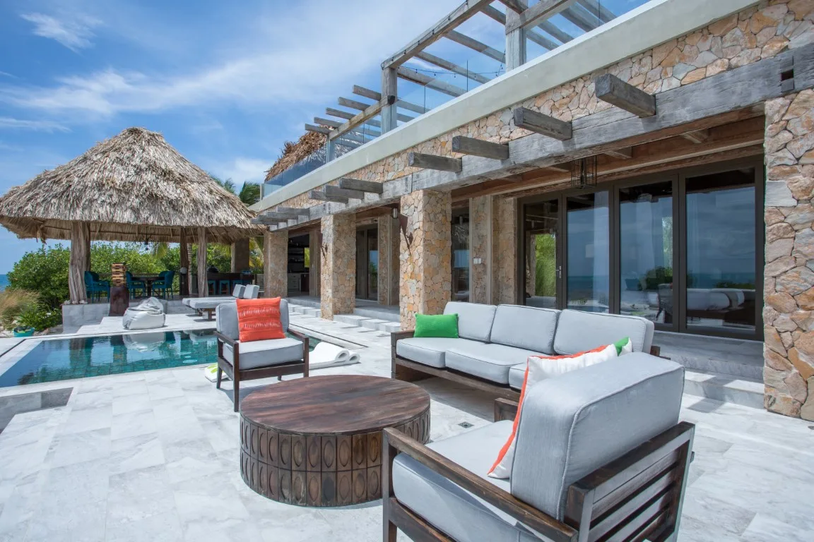 An outdoor patio with cushioned seating beside a swimming pool and stone-clad building.
