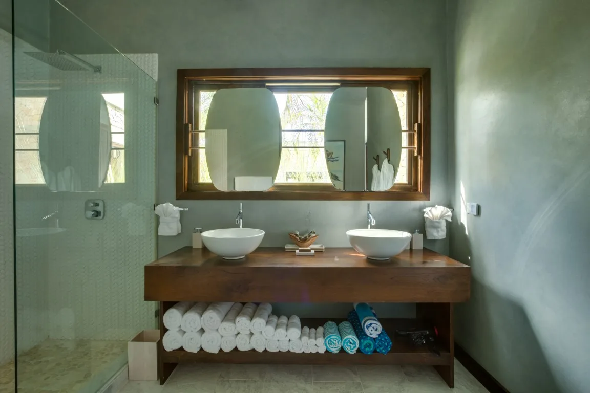 A bathroom vanity with two sinks, a wide mirror, and towels stored below.