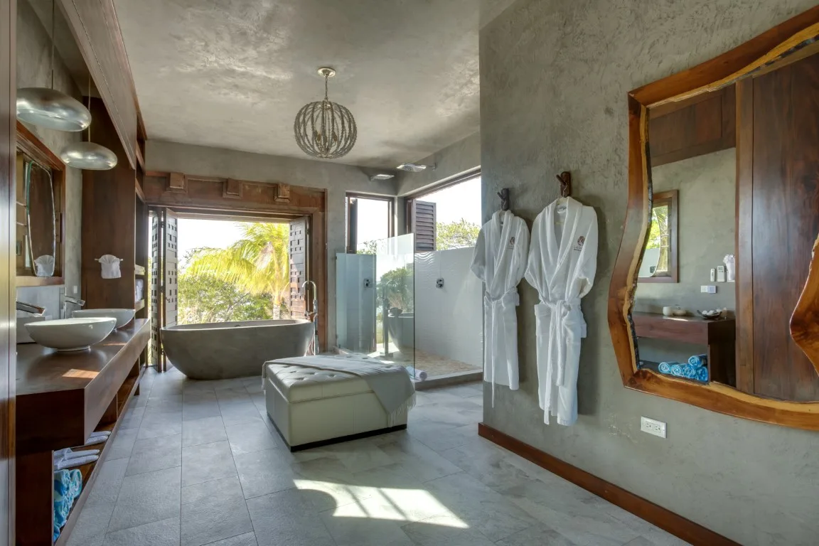 A spacious bathroom with a bathtub, glass shower, and two white robes.