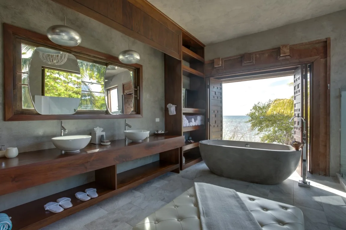 A bathroom vanity and bathtub sit beside an open doorway overlooking the water.