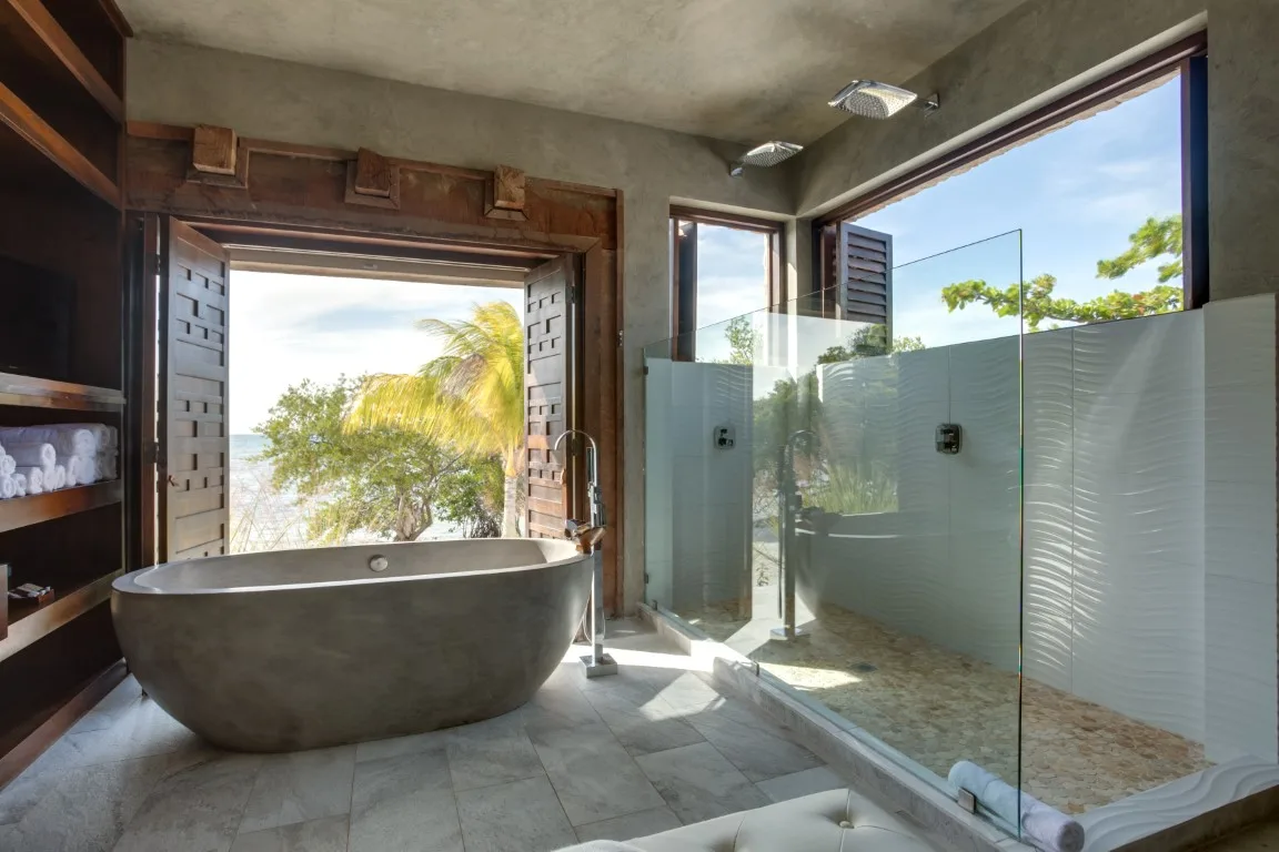 A bathroom with a freestanding bathtub and glass shower overlooking trees.