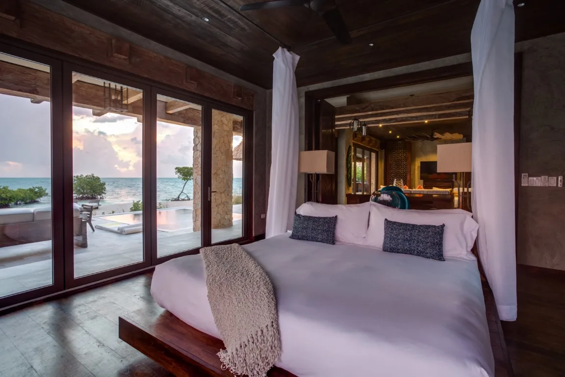 A bedroom with a large bed beside glass doors overlooking the water.