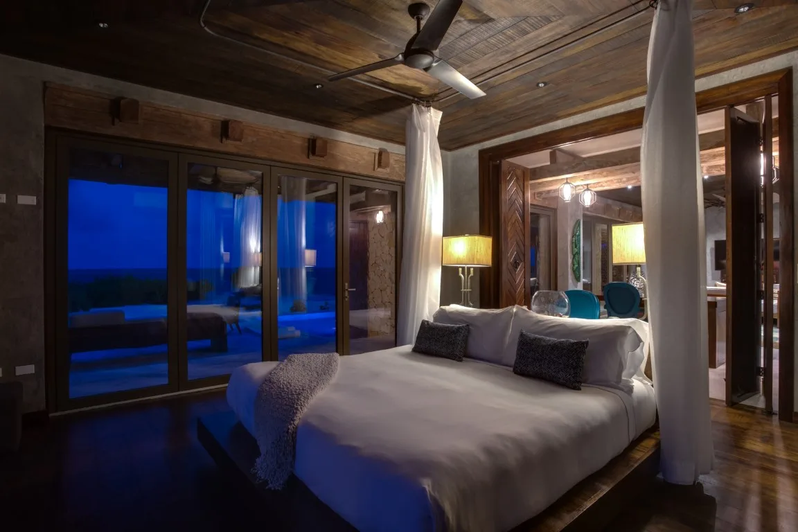 A bedroom with a large bed, bedside lamps, and glass doors opening to a balcony.