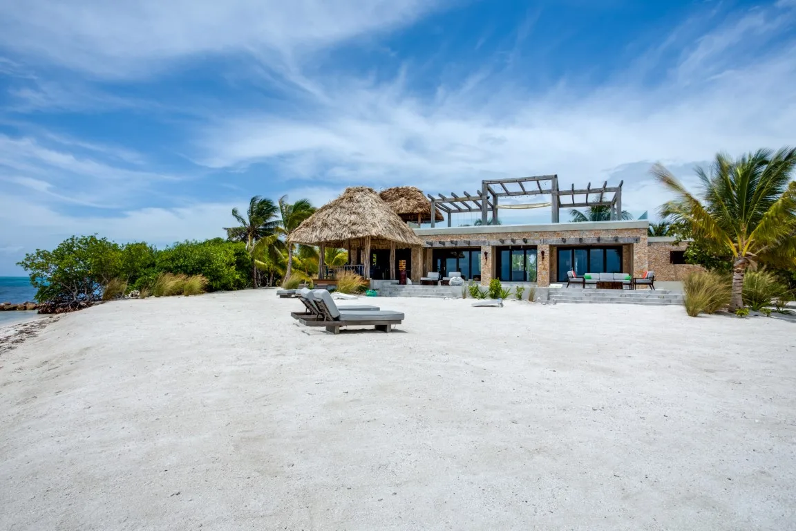 A modern beachfront building sits beside a broad pale sandy shore under a blue sky.