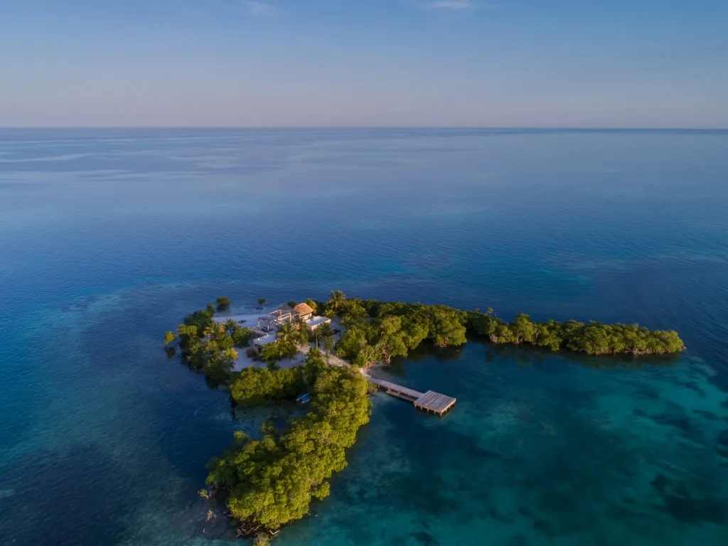 A small tropical island extends into clear blue water beneath a calm horizon.