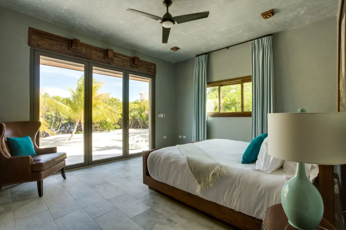 A bedroom with a bed, a chair, and large glass doors opening onto a garden.