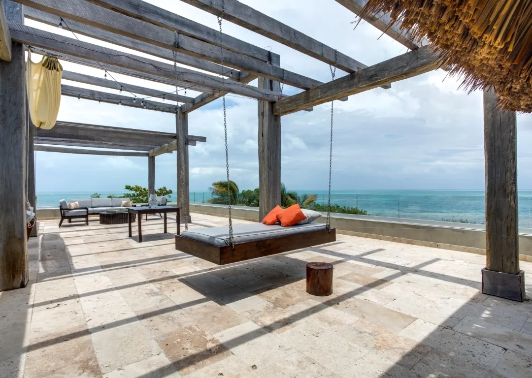 An open seaside terrace has a suspended wooden bench and views of the ocean.