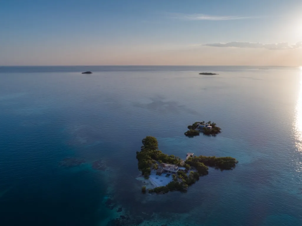 Small green islands sit in calm blue water beneath a bright sky.