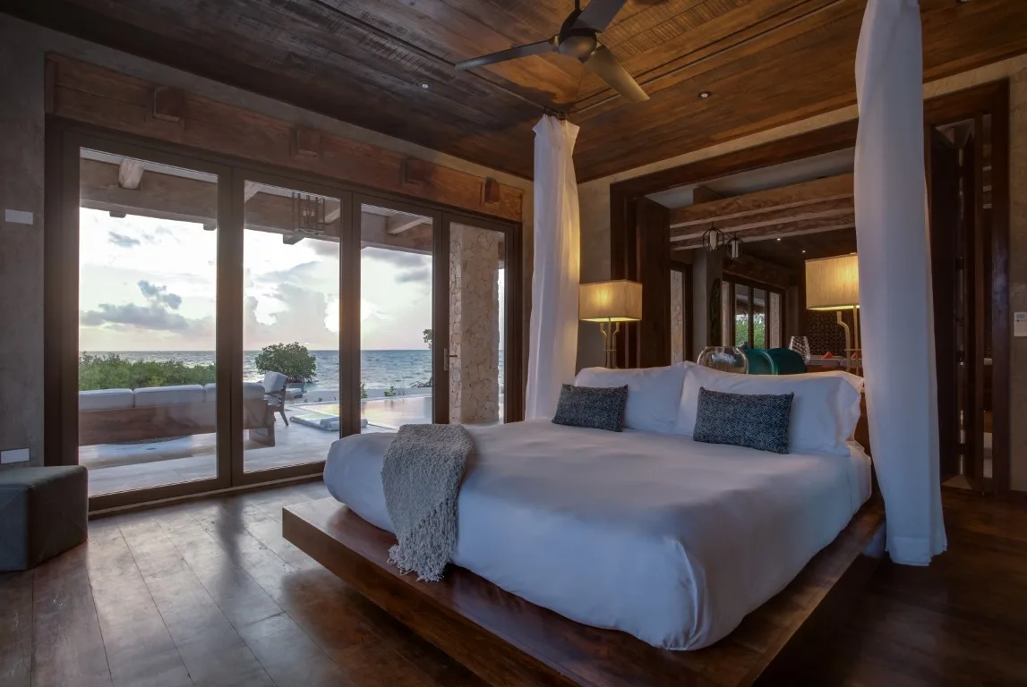 A bedroom with a large bed facing glass doors that open onto an ocean view.