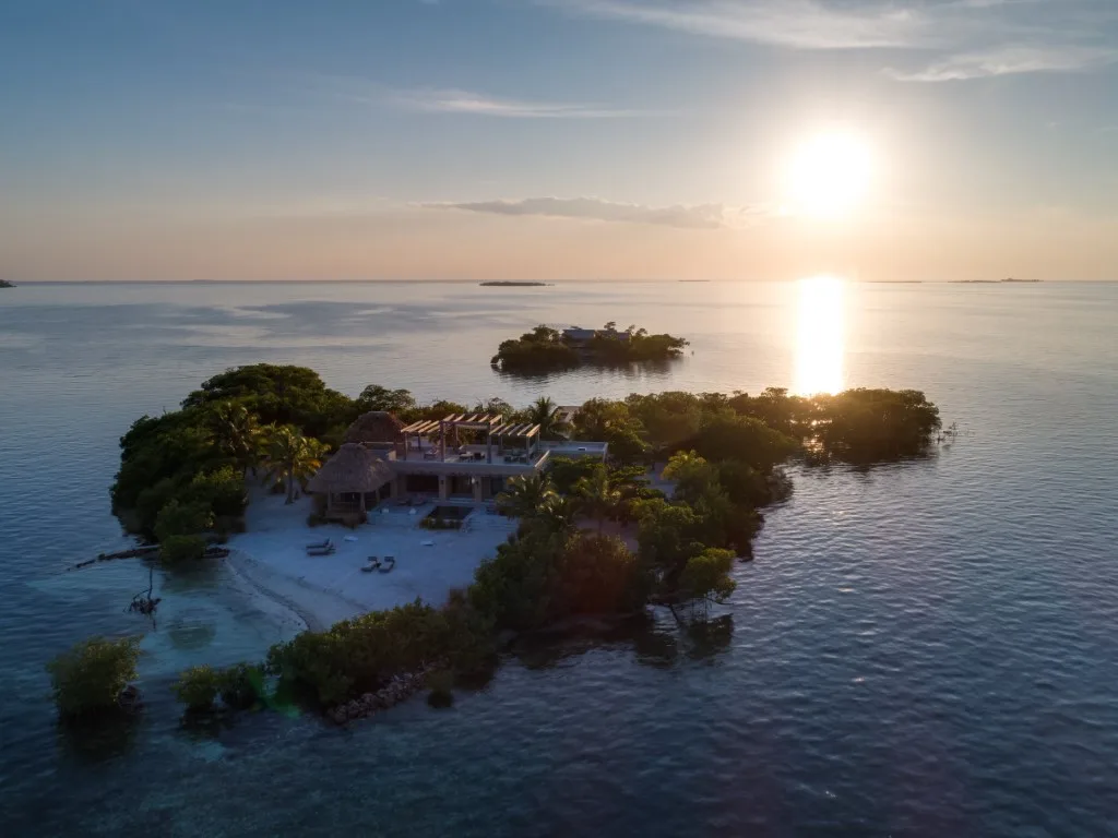 An aerial view of a small tropical island surrounded by calm water at sunset.
