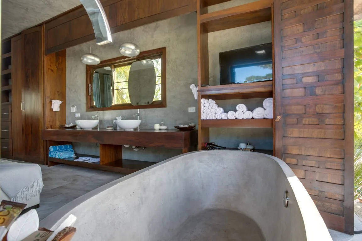 A bathroom features a freestanding bathtub, double sinks, and wooden shelving.