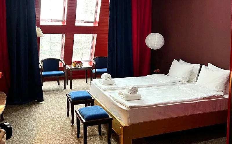 Representative hotel space: A bedroom with two beds, blue seating, and tall windows.