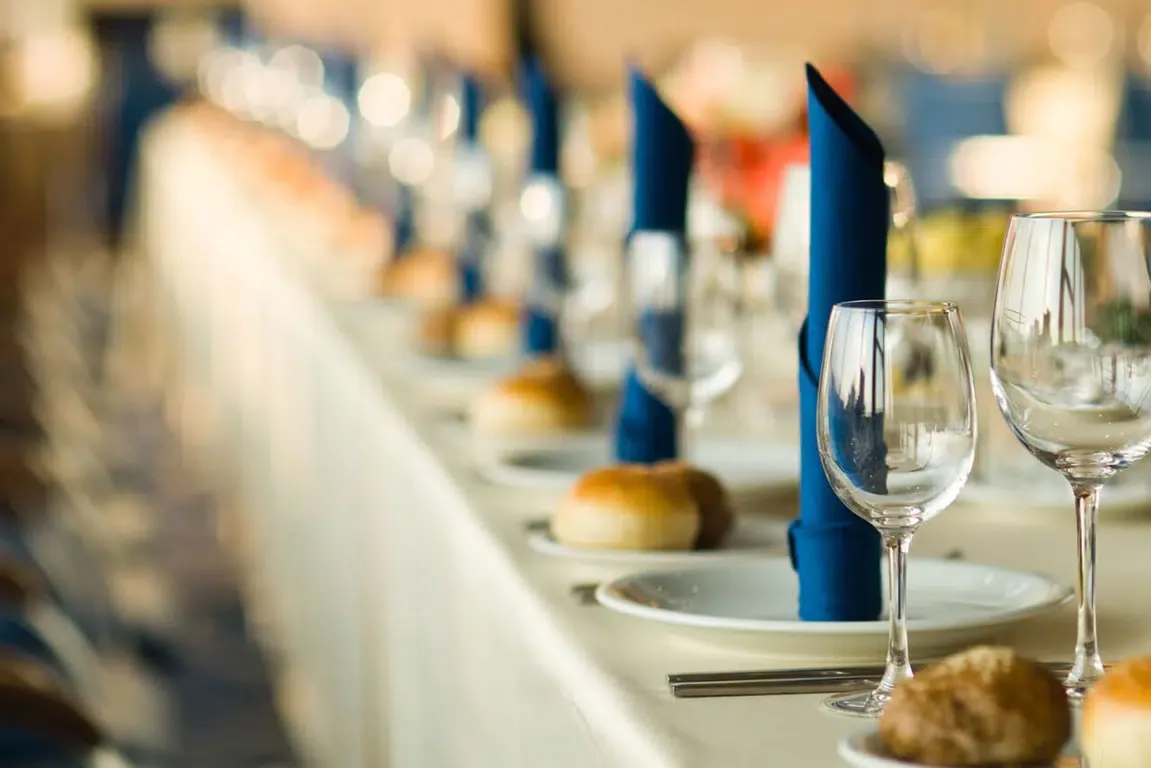Representative hotel space: A dining table is set with plates, bread, glasses, and folded blue napkins.