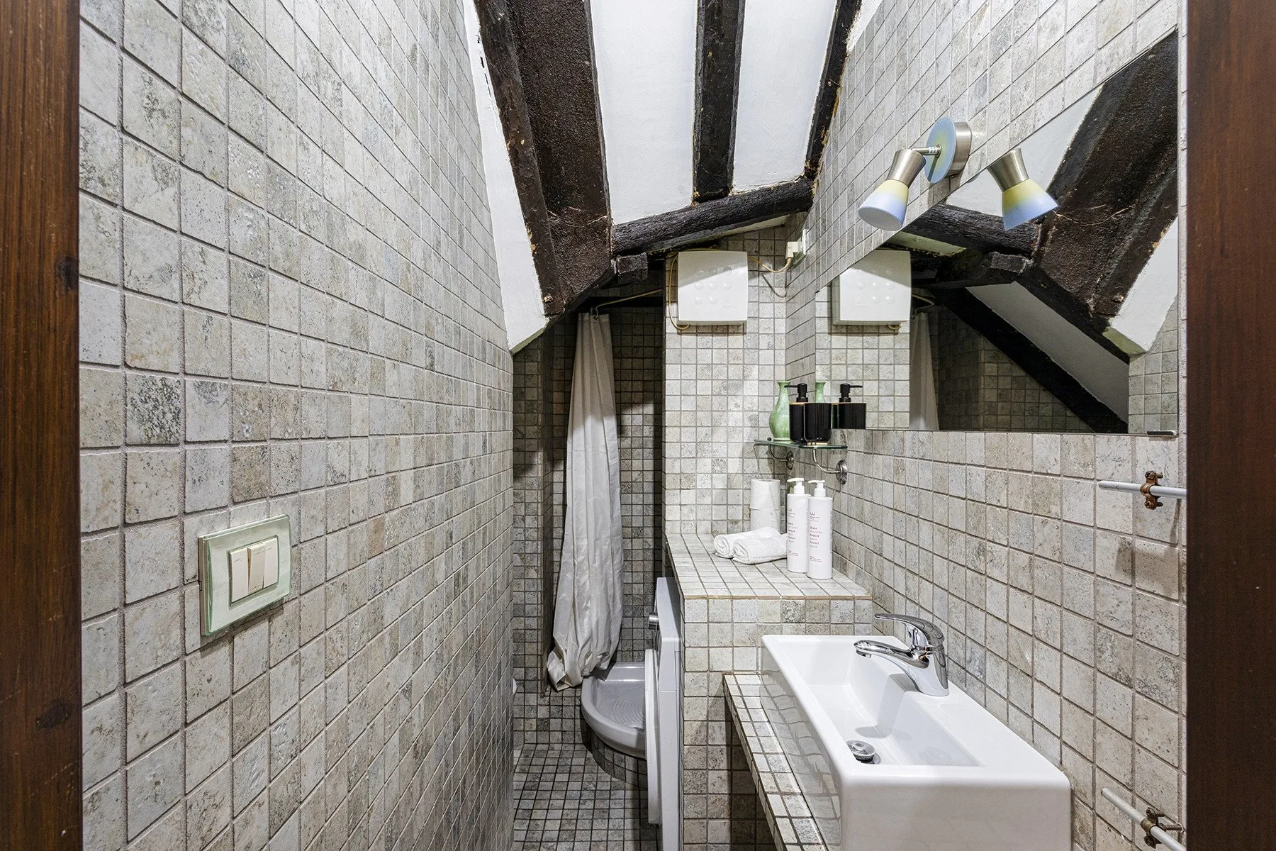 Un baño alicatado con bañera, lavabo y vigas oscuras a la vista.