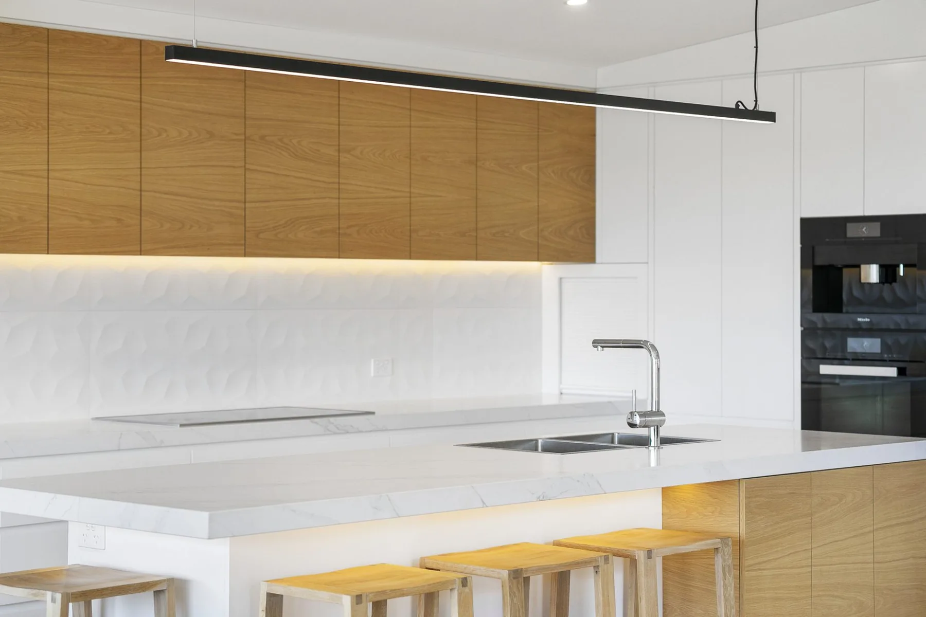 Una cocina moderna con una isla blanca, gabinetes de madera y taburetes.