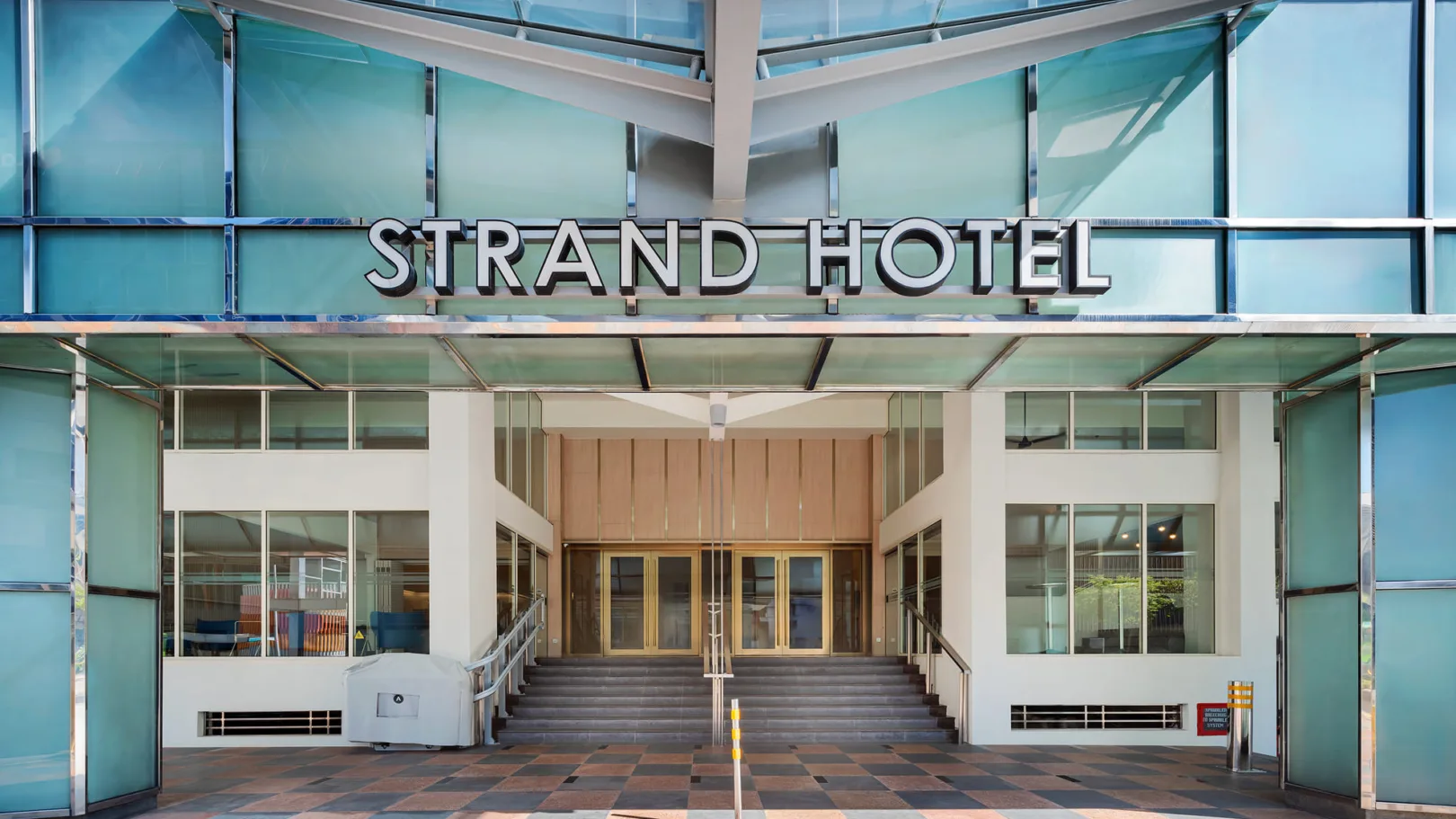 Representative hotel space: The Strand Hotel entrance has glass walls and a covered walkway.