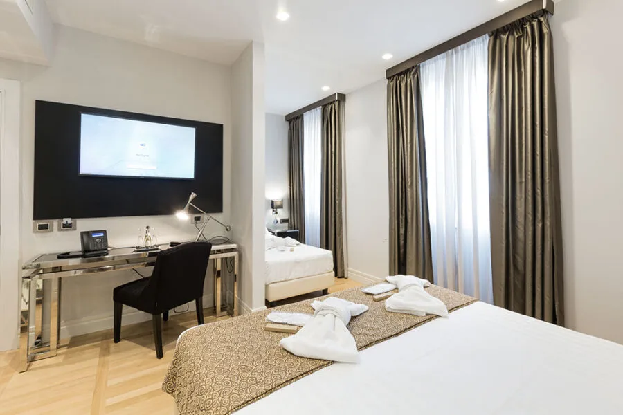 Representative hotel space: A bedroom with a desk and seating beside tall curtained windows.
