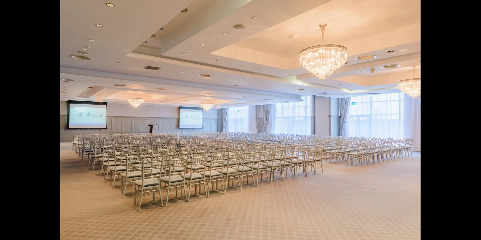 Representative hotel space: A large meeting room is arranged with rows of chairs beneath chandeliers.