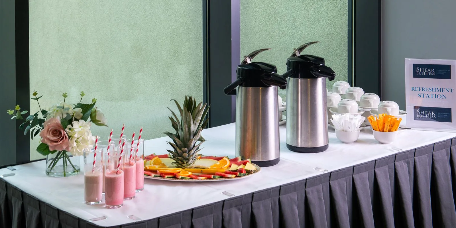 Representative hotel space: A refreshment station displays beverage dispensers, pink drinks, and fruit.