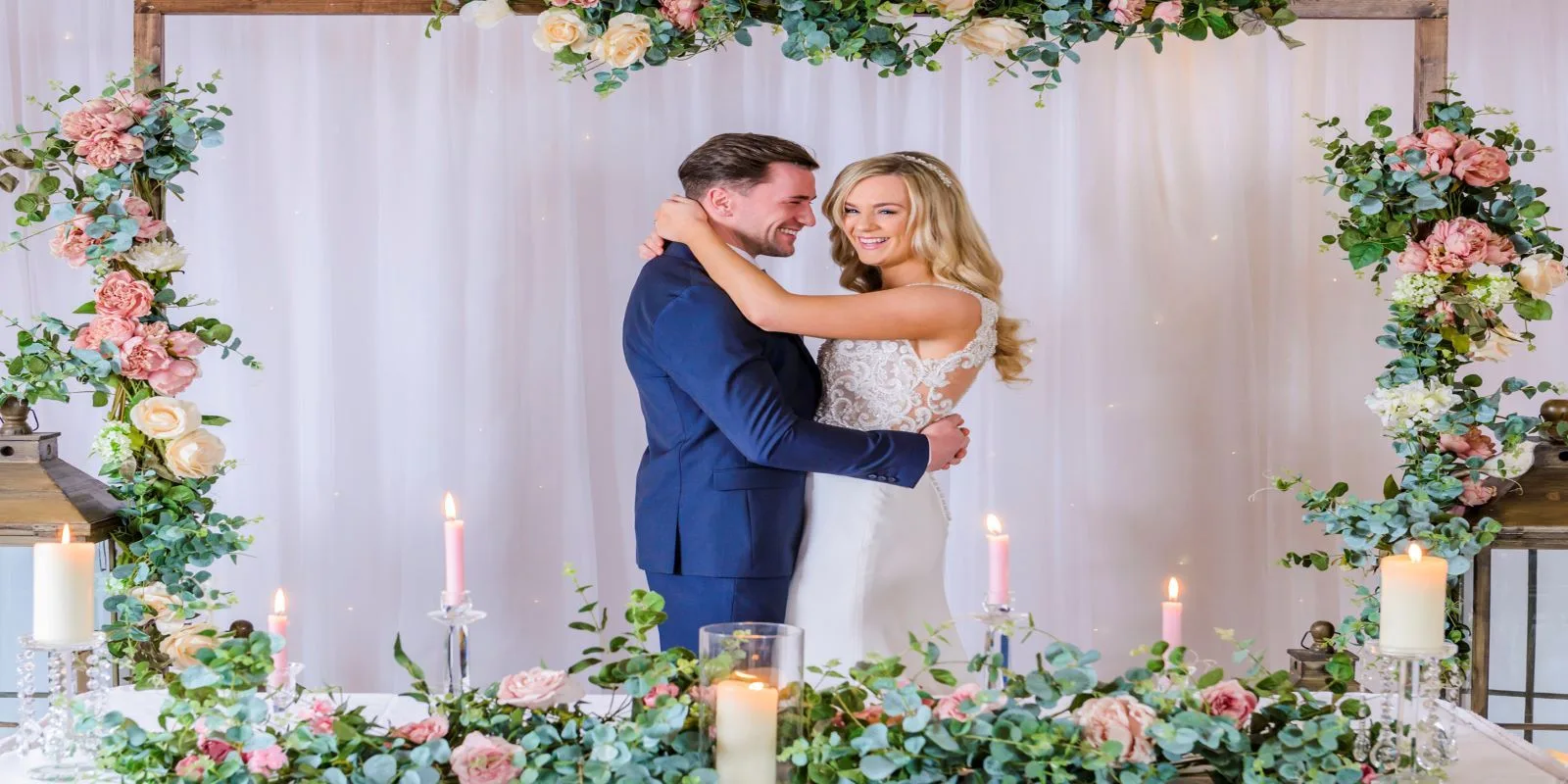 Representative hotel space: A couple embraces beneath a floral wedding arch.