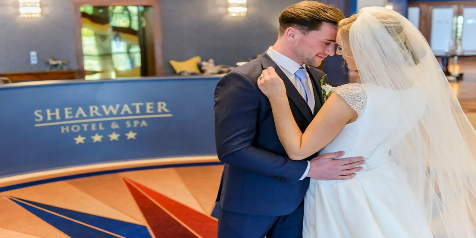Representative hotel space: A couple embraces at a hotel reception desk.