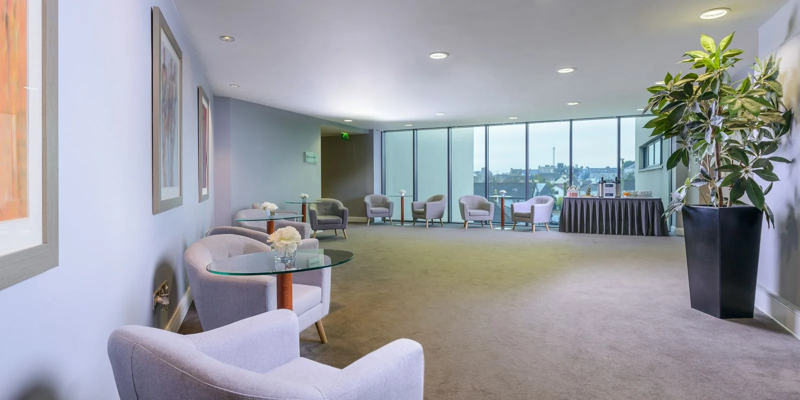 Representative hotel space: A bright hotel lounge has seating beside large windows and a potted plant.