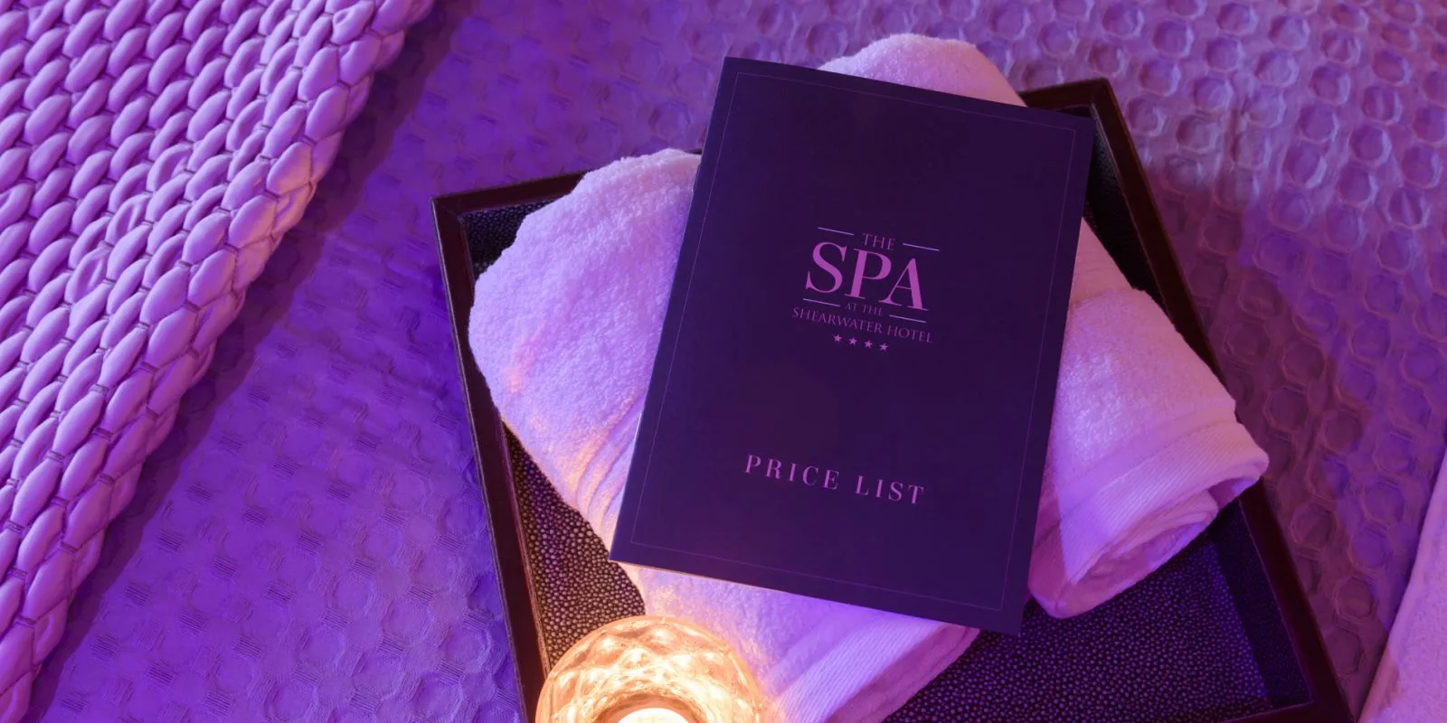 Representative hotel space: A spa tray holds folded towels and a dark price list under purple lighting.