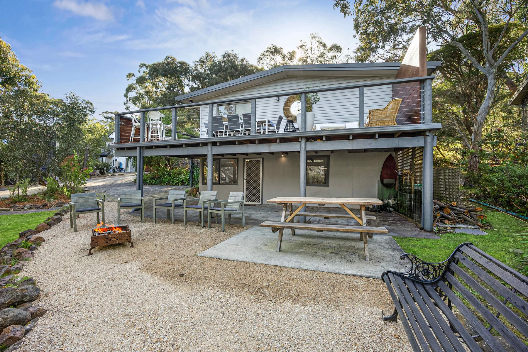 A raised house overlooks an outdoor gravel patio with seating and a picnic table.