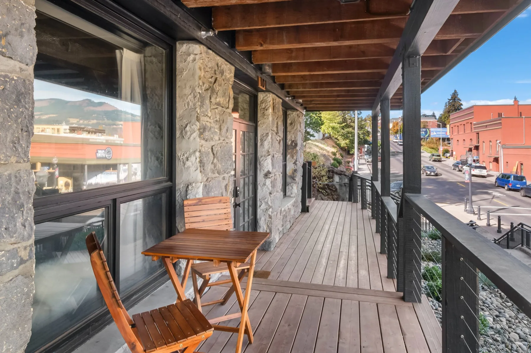 Representative hotel space: A covered wooden deck runs alongside a stone building, with a small table and seating.