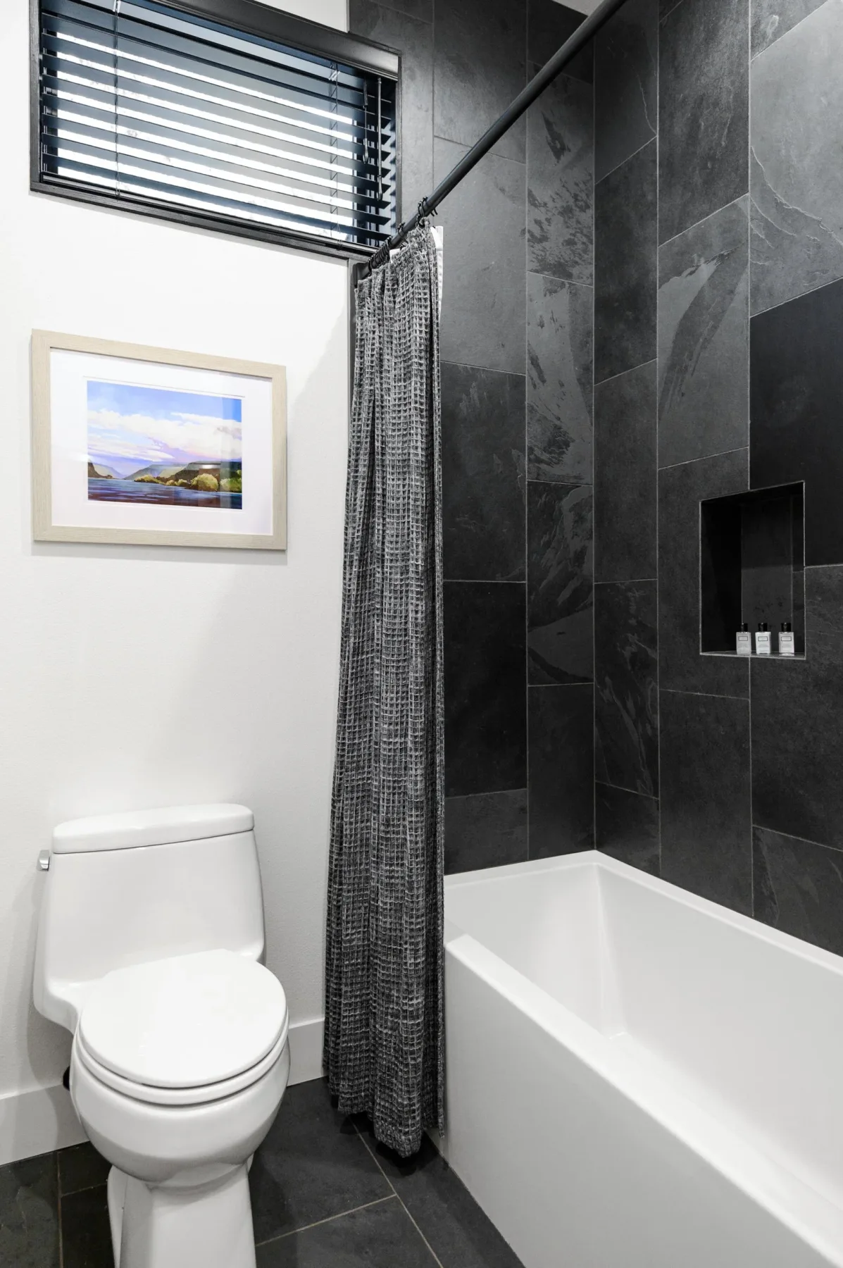 Representative hotel space: Bathroom with a bathtub, toilet, and dark tiled walls.