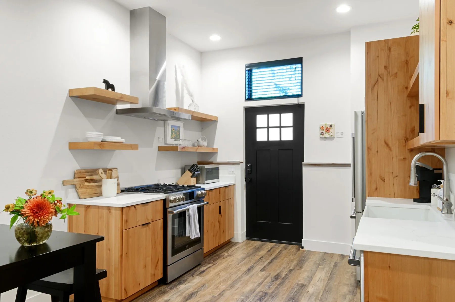 Representative hotel space: A bright kitchen with wood cabinetry, open shelves, and a black door.