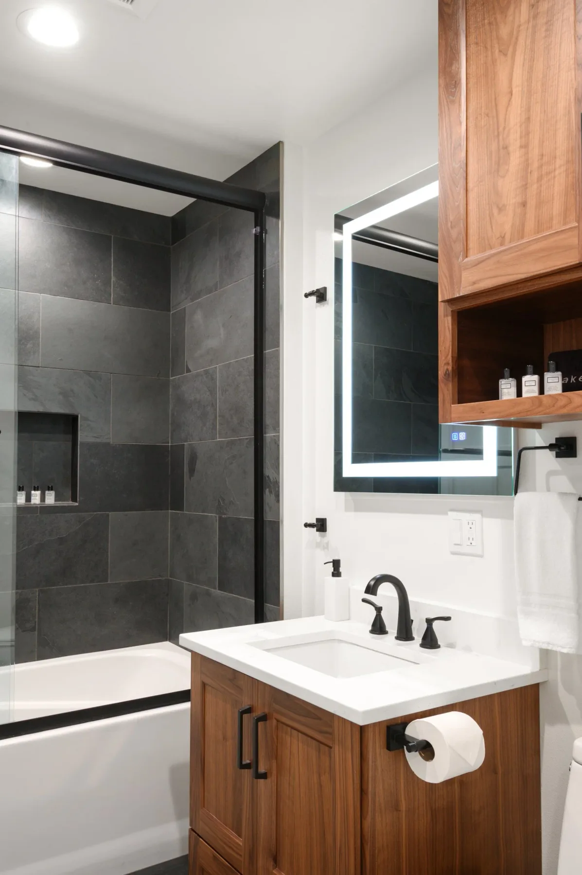 Representative hotel space: A bathroom with a dark tiled shower, white tub, and wood vanity.