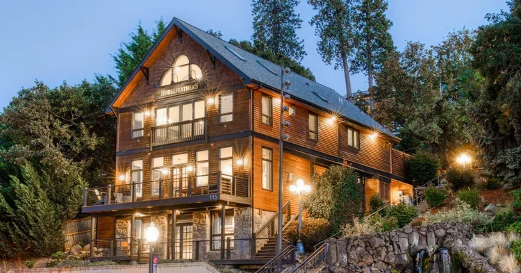 Representative hotel space: A large timber-clad building glows with warm lights among trees at dusk.
