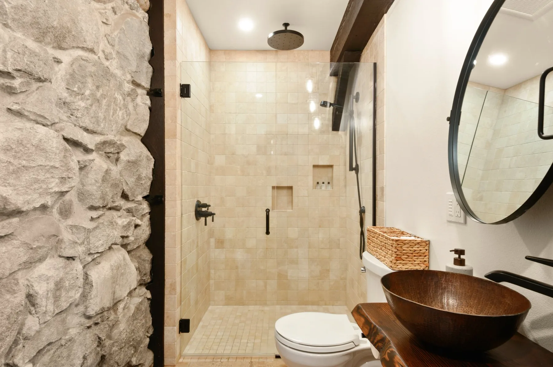 Representative hotel space: A bathroom features a glass shower, a vessel sink, and an exposed stone wall.