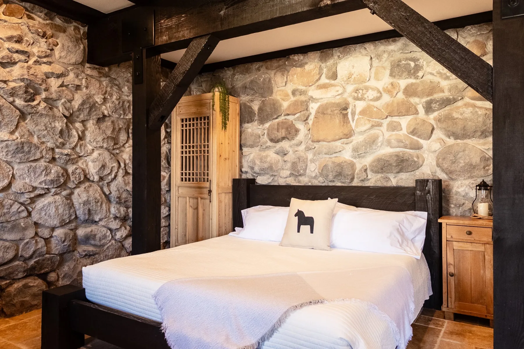 Representative hotel space: A bedroom with a bed against a stone wall and dark wooden beams.