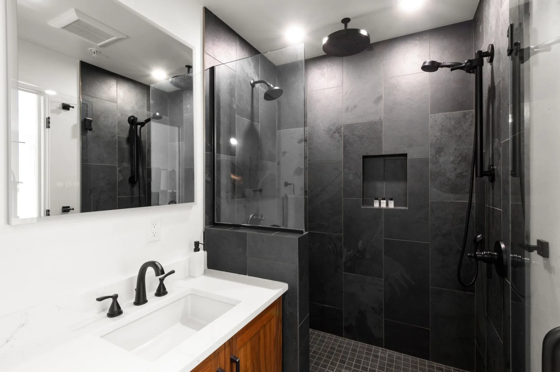 Representative hotel space: A bathroom with a white sink and a dark tiled shower area.