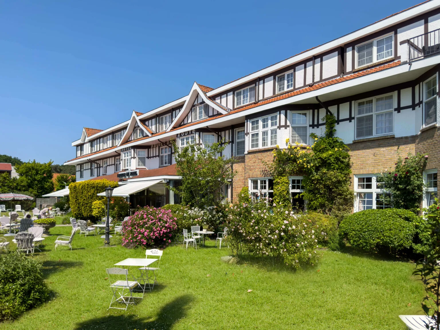 Espacio representativo del hotel: Un edificio hotelero de varias plantas da a un césped verde con asientos al aire libre.