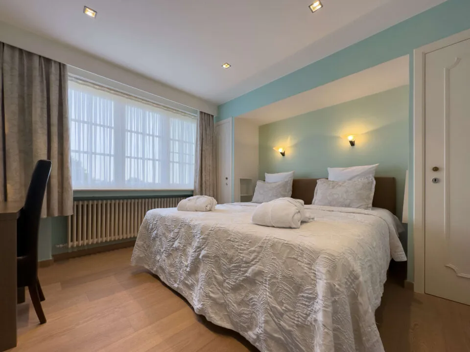 Espacio representativo del hotel: Un dormitorio con una cama doble junto a una pared verde azulado claro.