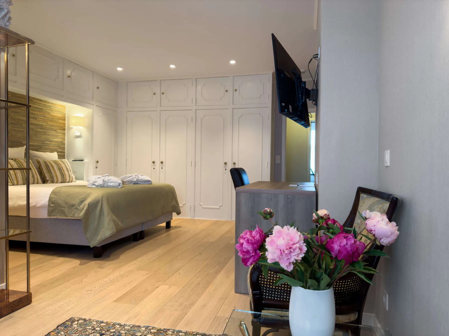 Espacio representativo del hotel: Dormitorio con una cama hecha, armarios empotrados y flores en primer plano.