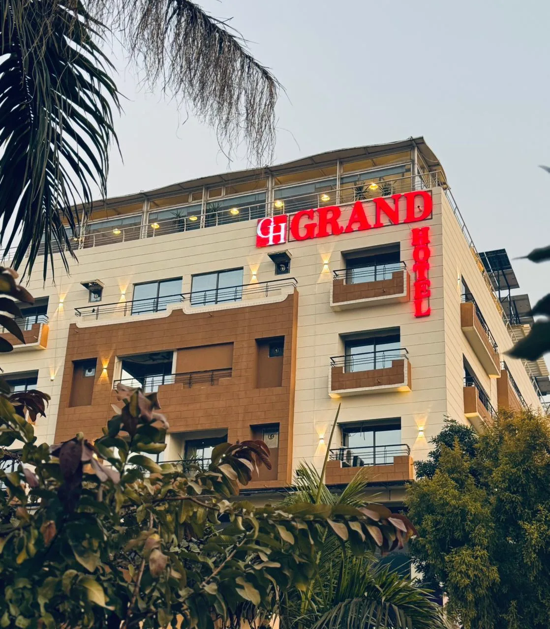 Espacio representativo del hotel: Un edificio hotelero de varios pisos con letrero iluminado y árboles frondosos al frente.