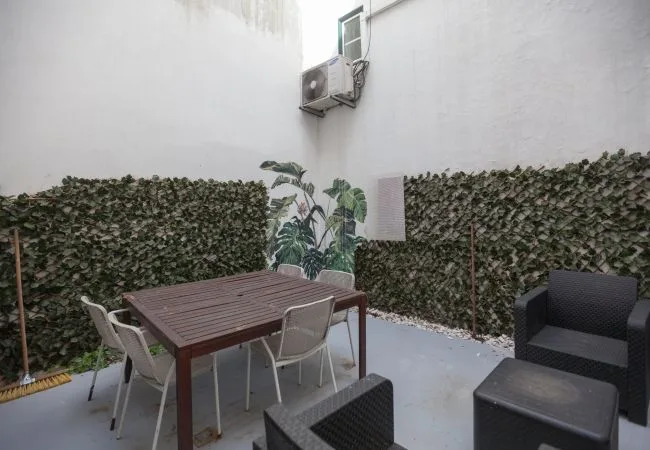 A small outdoor patio with a dining table, chairs, and dark seating.