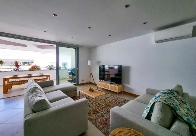 A bright living room with seating, a television, and sliding glass doors opening to a patio.