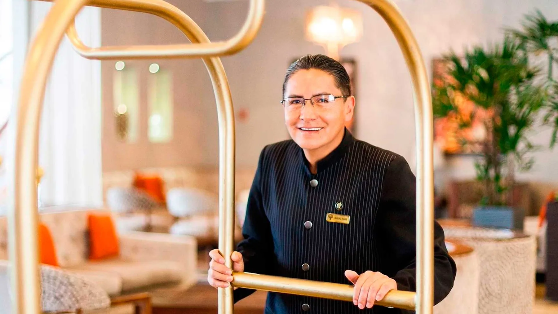 Representative hotel space: A hotel staff member stands beside a brass luggage cart in a lounge.