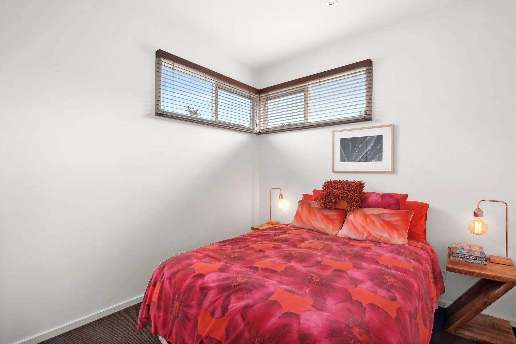 Un dormitorio con una cama vestida de rojo estampado y ventanas en la esquina.