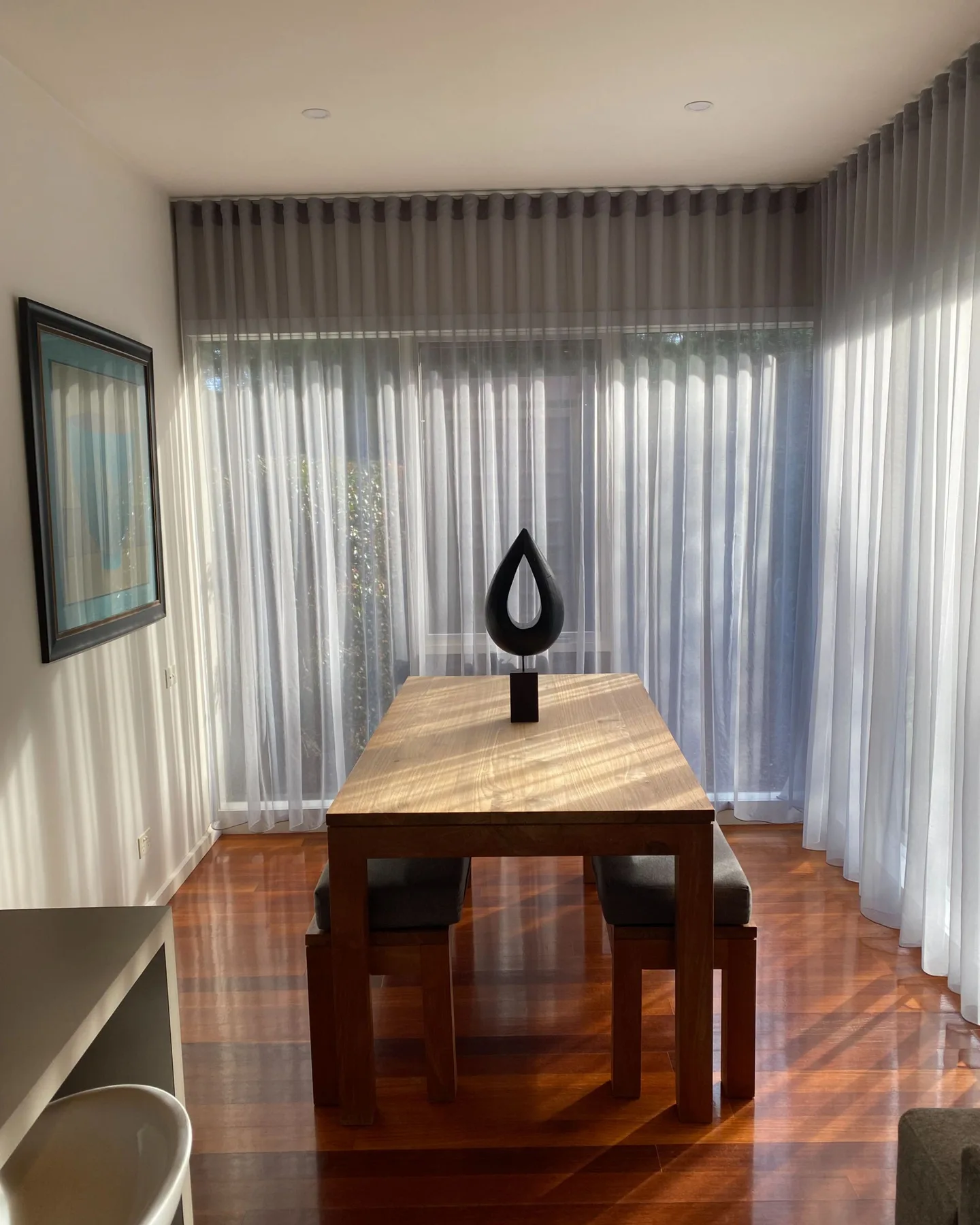 Comedor con una mesa de madera frente a cortinas translúcidas.