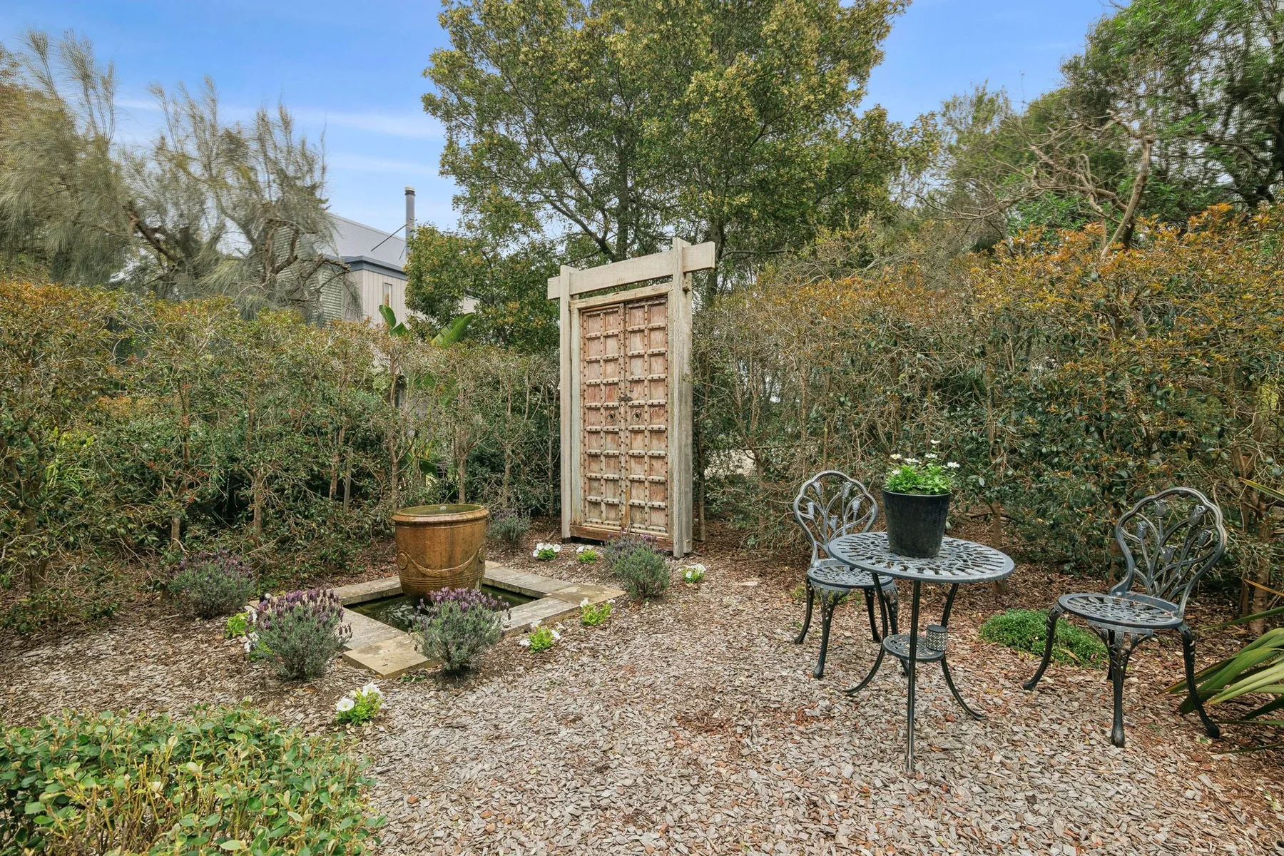 Un jardín de grava con una celosía de madera, plantas en macetas y asientos al aire libre.