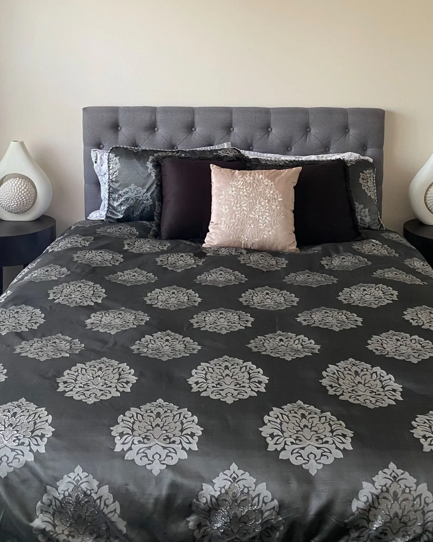 Un dormitorio con ropa de cama estampada y un cabecero gris capitoné.