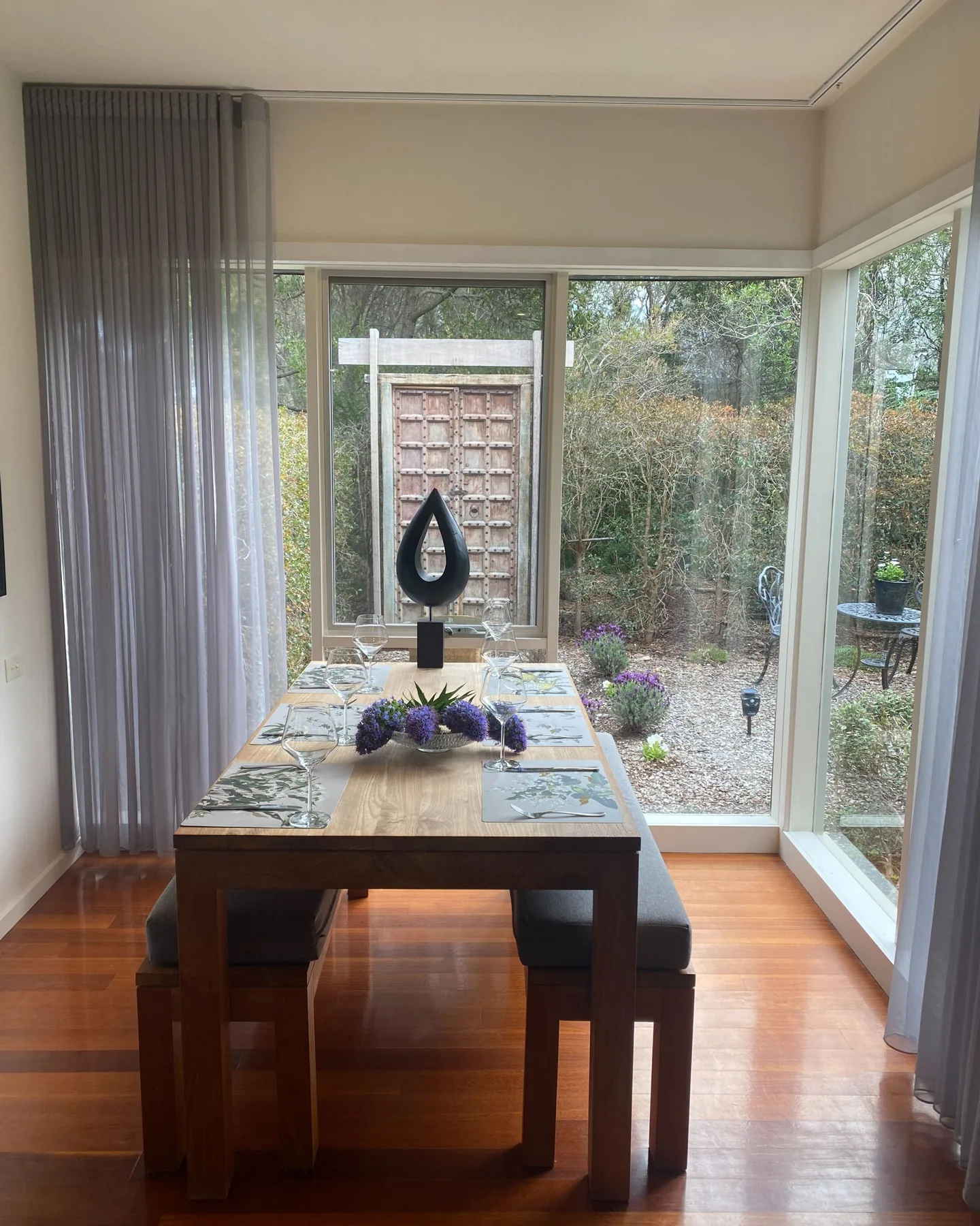 Comedor con una mesa de madera junto a ventanales que dan a un jardín.