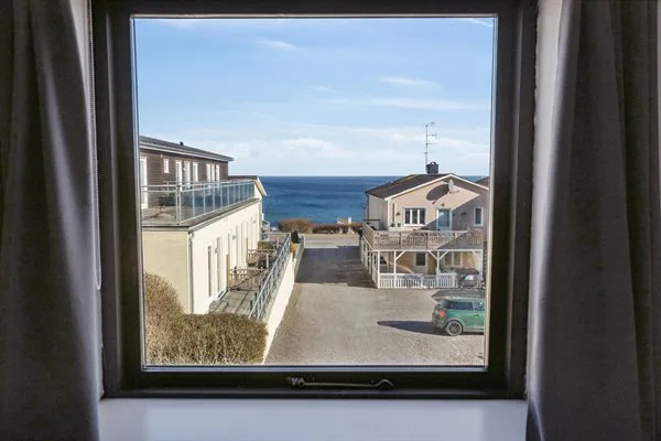 Una ventana enmarca edificios cercanos y una vista del mar.