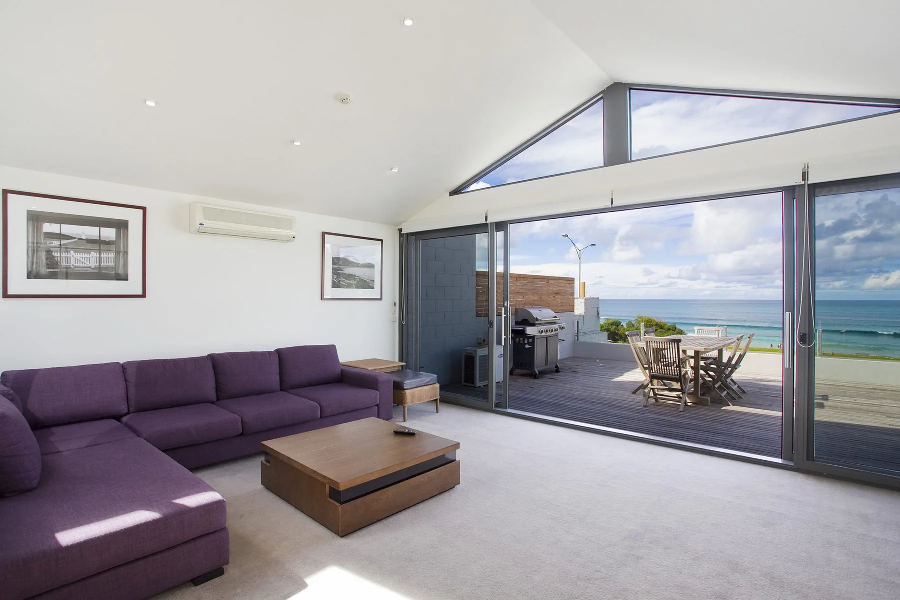 A bright living room opens onto a deck with outdoor seating and ocean views.